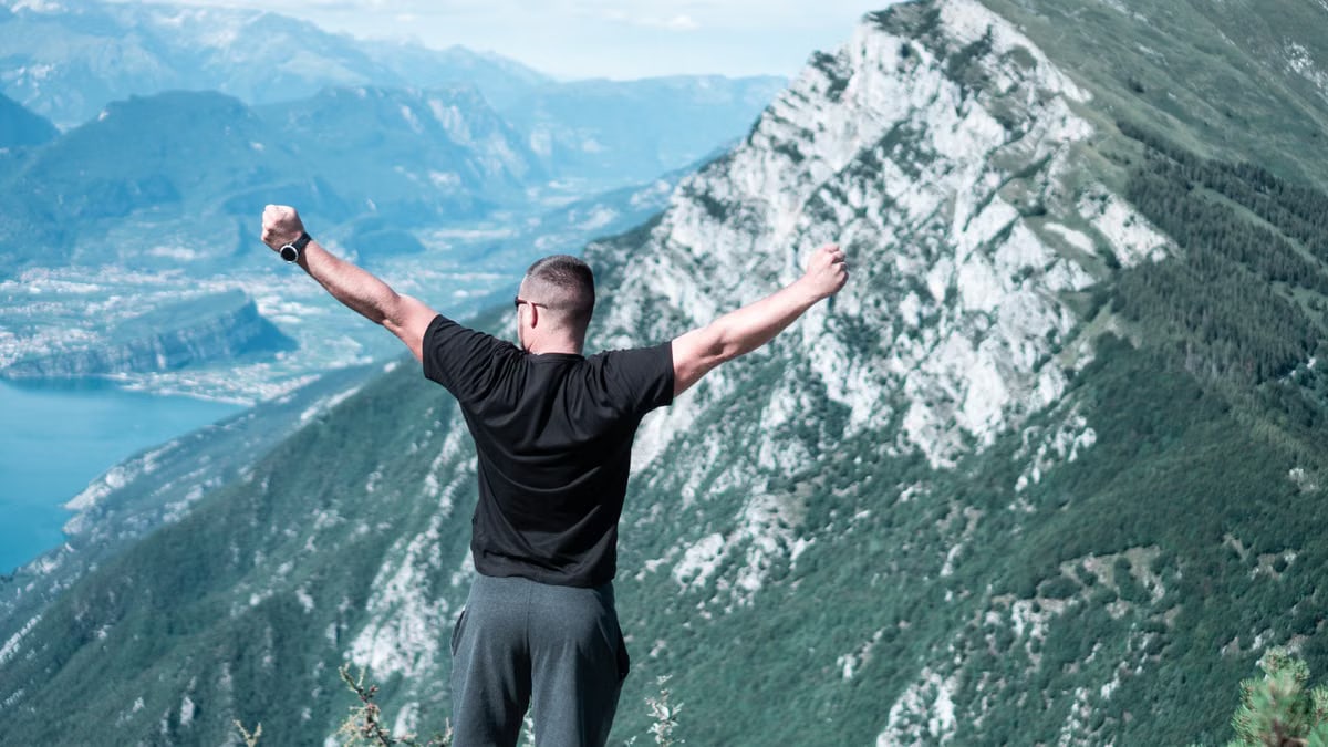 Man standing with arms raised in celebration overlooking a breathtaking mountain landscape.
